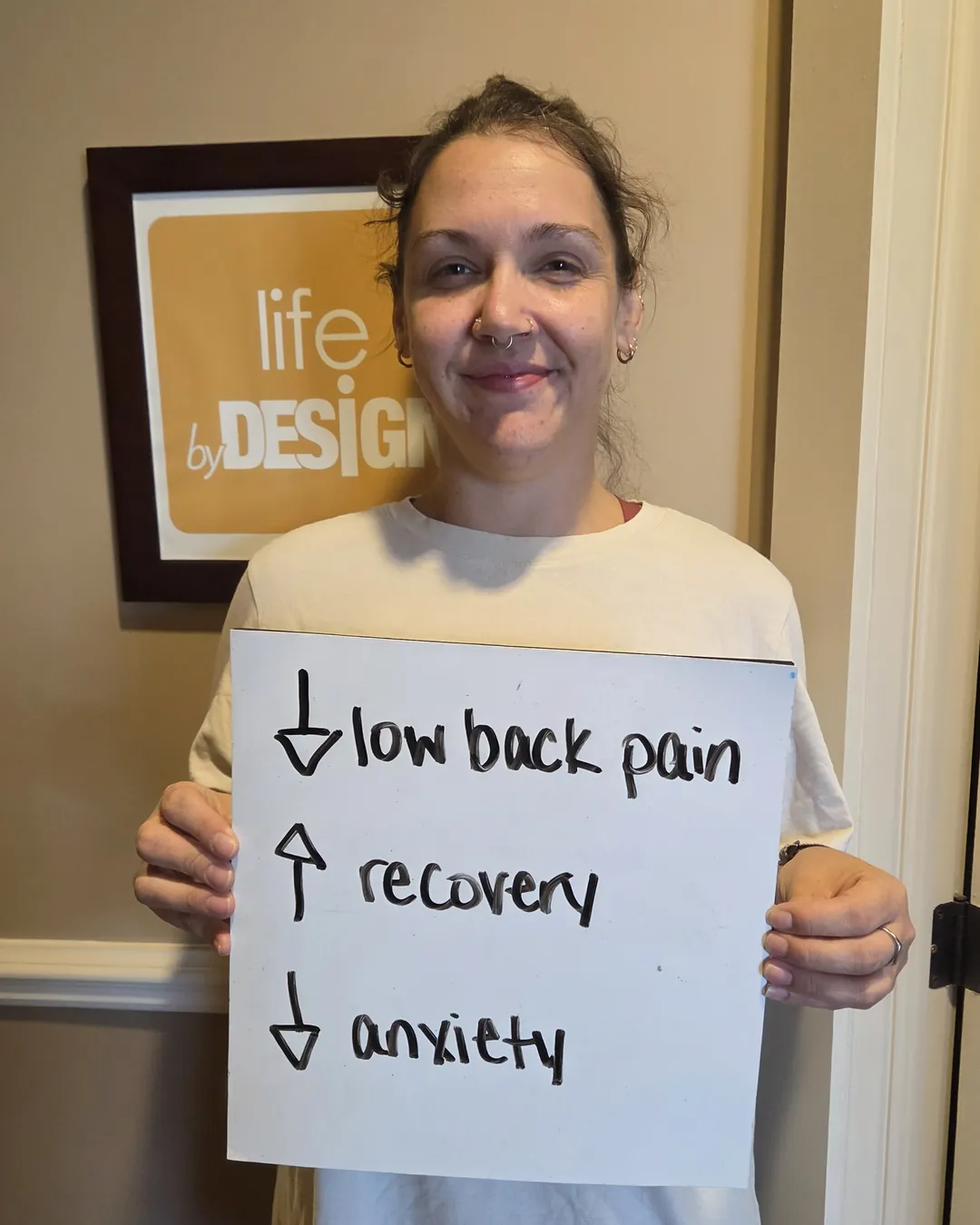 Patient at Synergy Wellness Group, a Kanata chiropractic clinic, holding a sign that reads "less low back pain, better recovery, less anxiety"