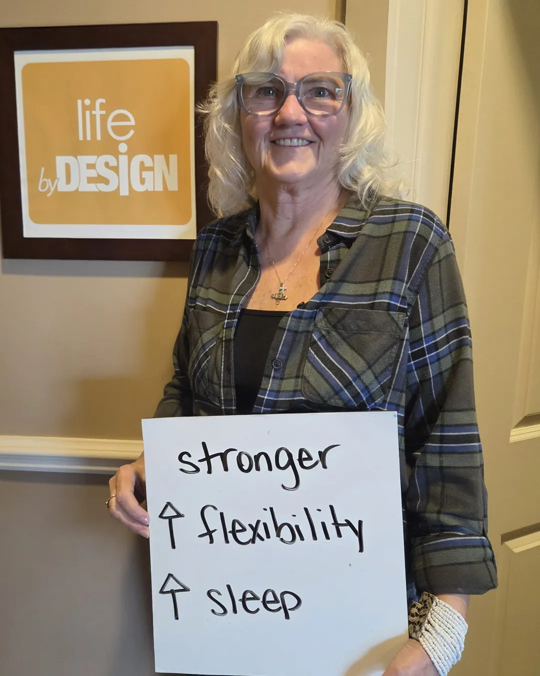 Smiling patient in the Kanata chiropractic office holding a sign that reads "stronger, more flexibility, better sleep"